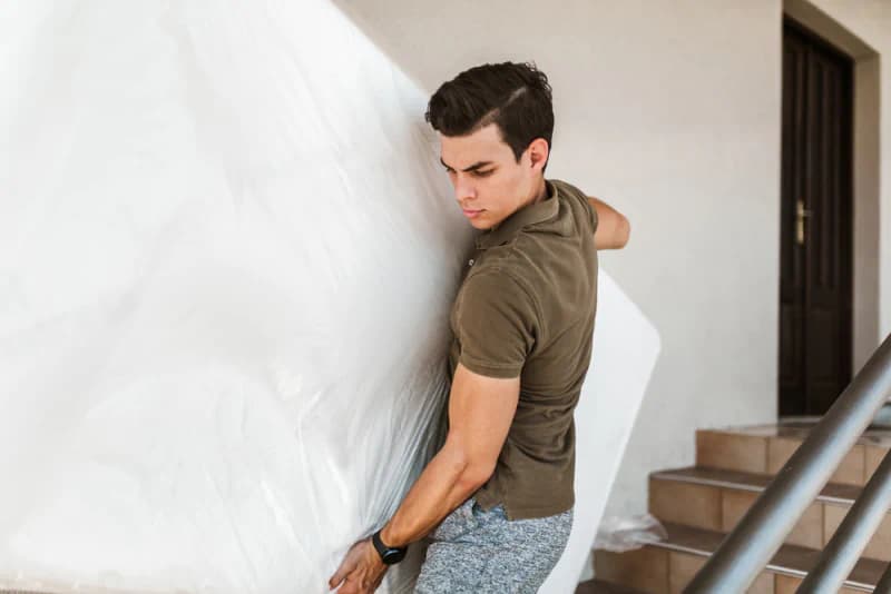 Man carrying a protected mattress downstairs to store it