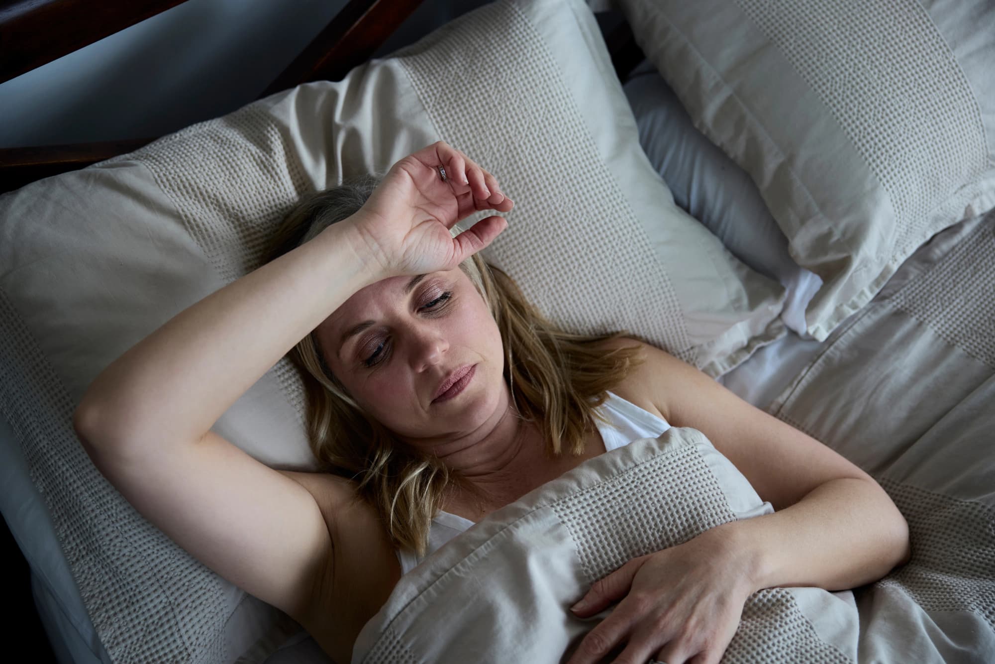 Woman with her arm over forehead can’t sleep.