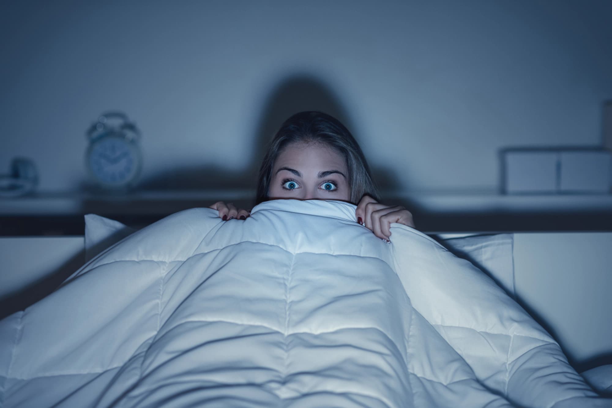 Woman scared under her bed covers.