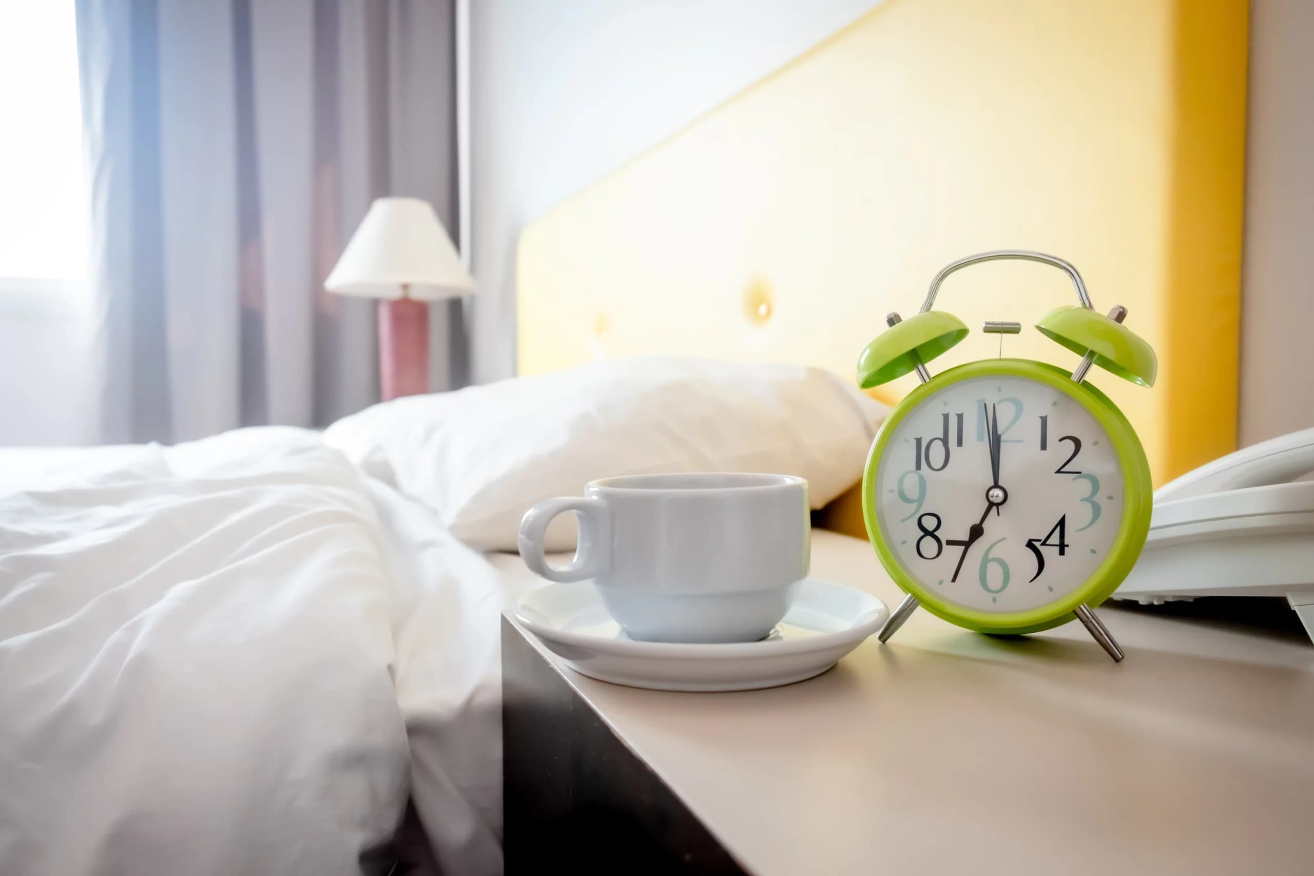 Coffee cup next to bed and an alarm clock.