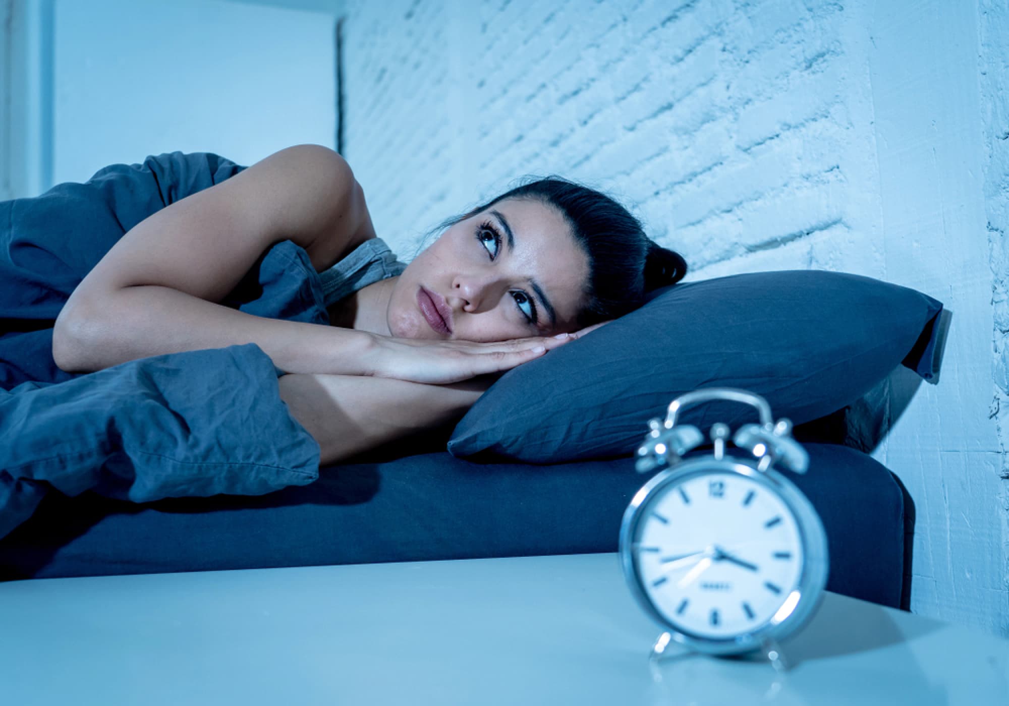 Woman lying awake in bed next to a clock.