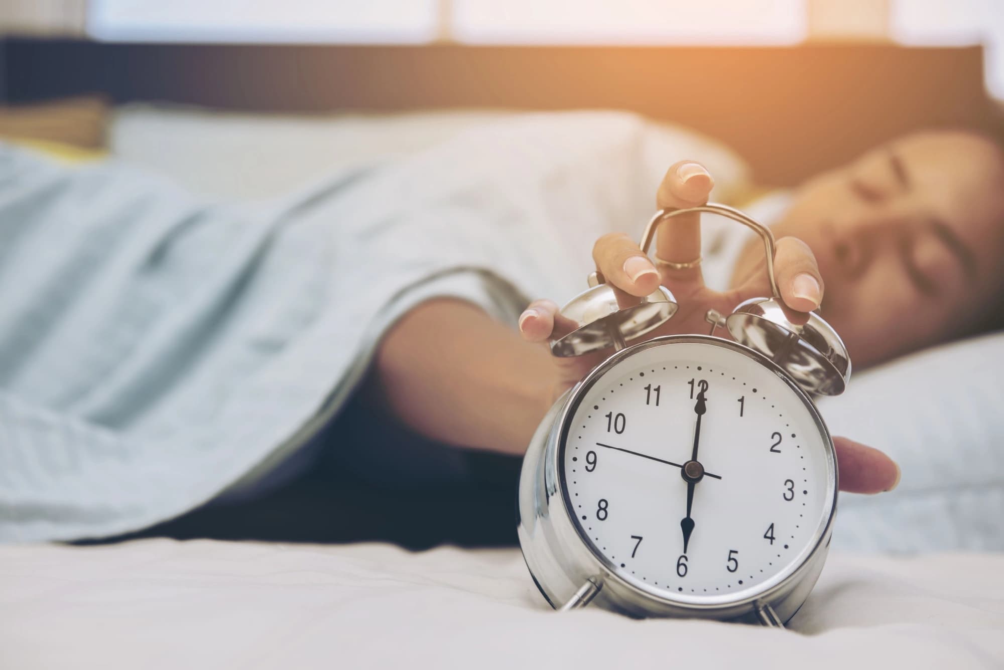 Tired woman in bed touching her alarm clock