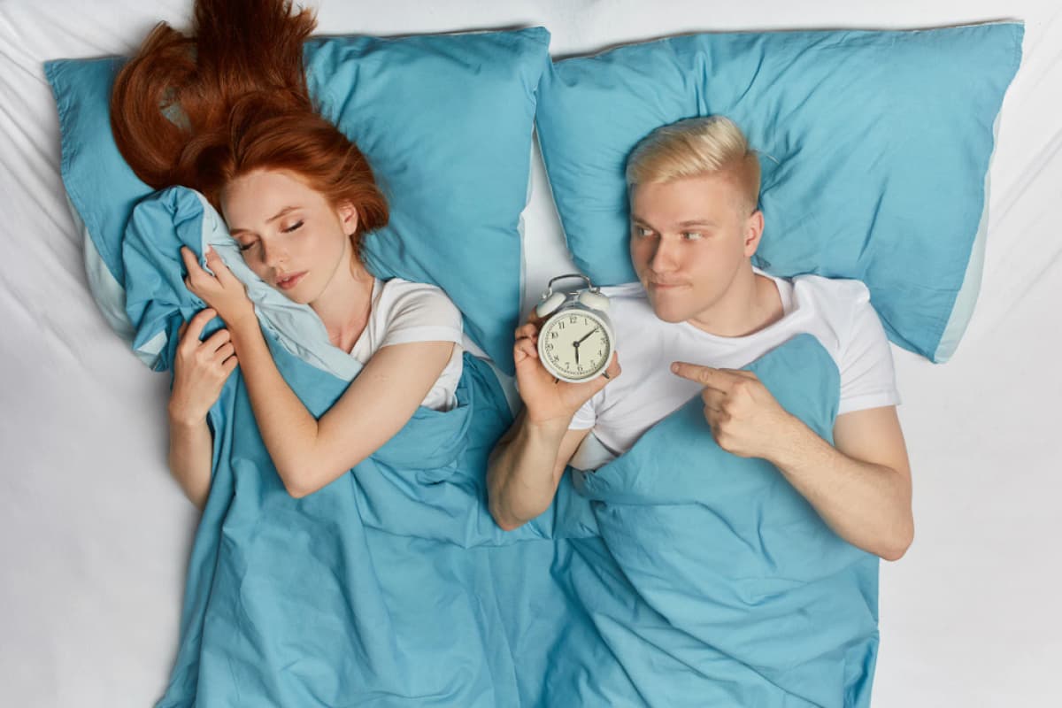 Man holding an alarm clock while a woman is still sleeping