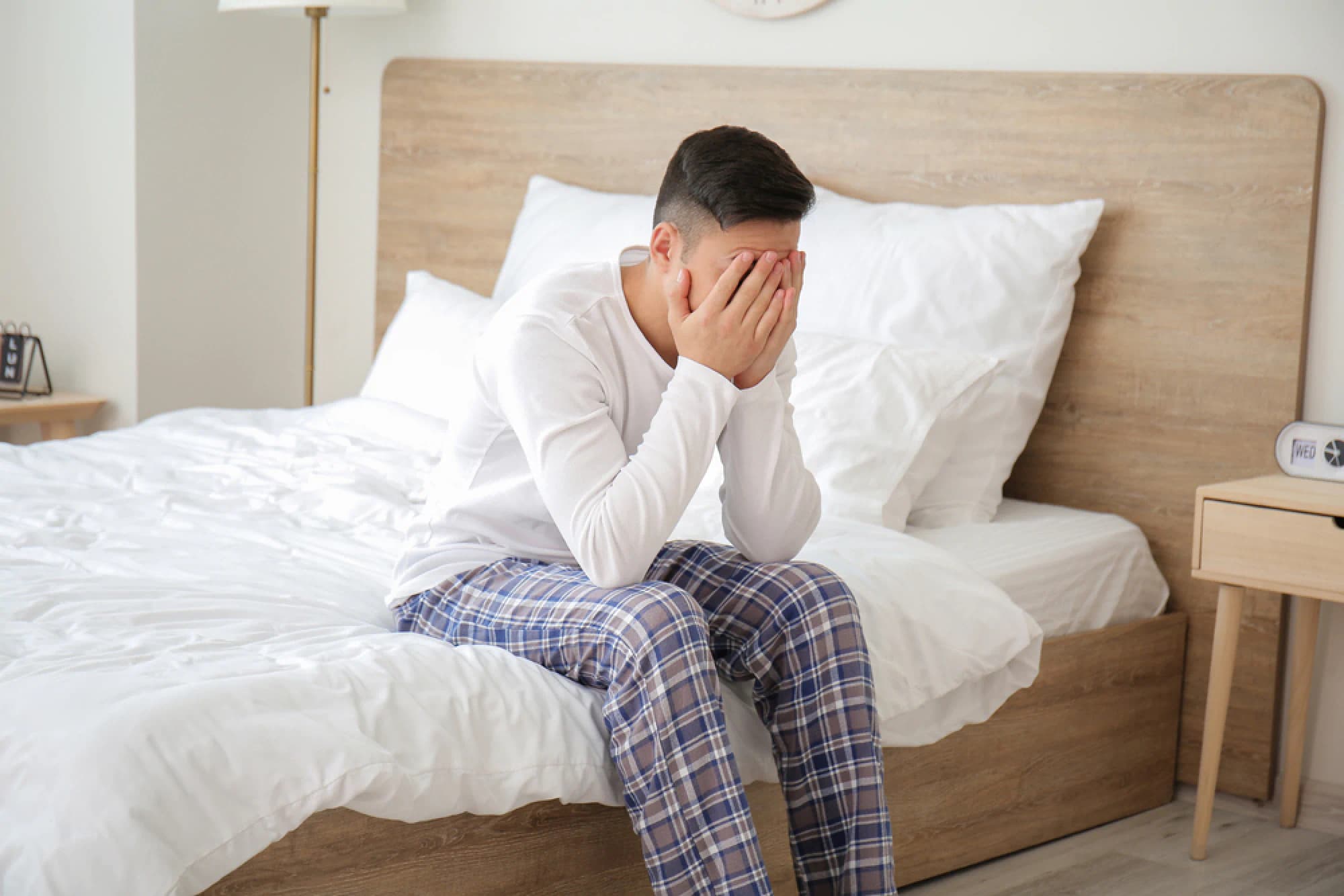 Man sitting on the edge of his bed with his head in his hands