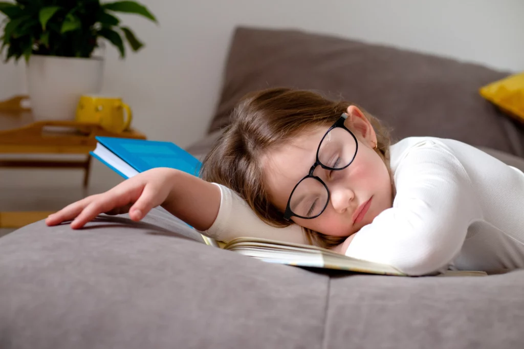 Young girl with glasses falls asleep on bed.