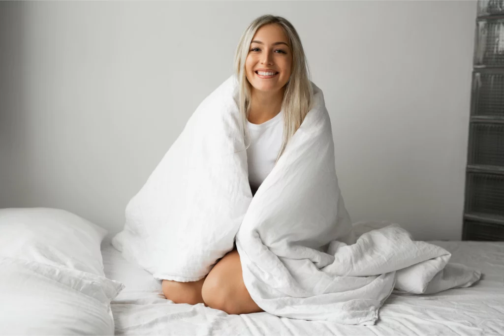 Woman sitting on white blanket in bed.