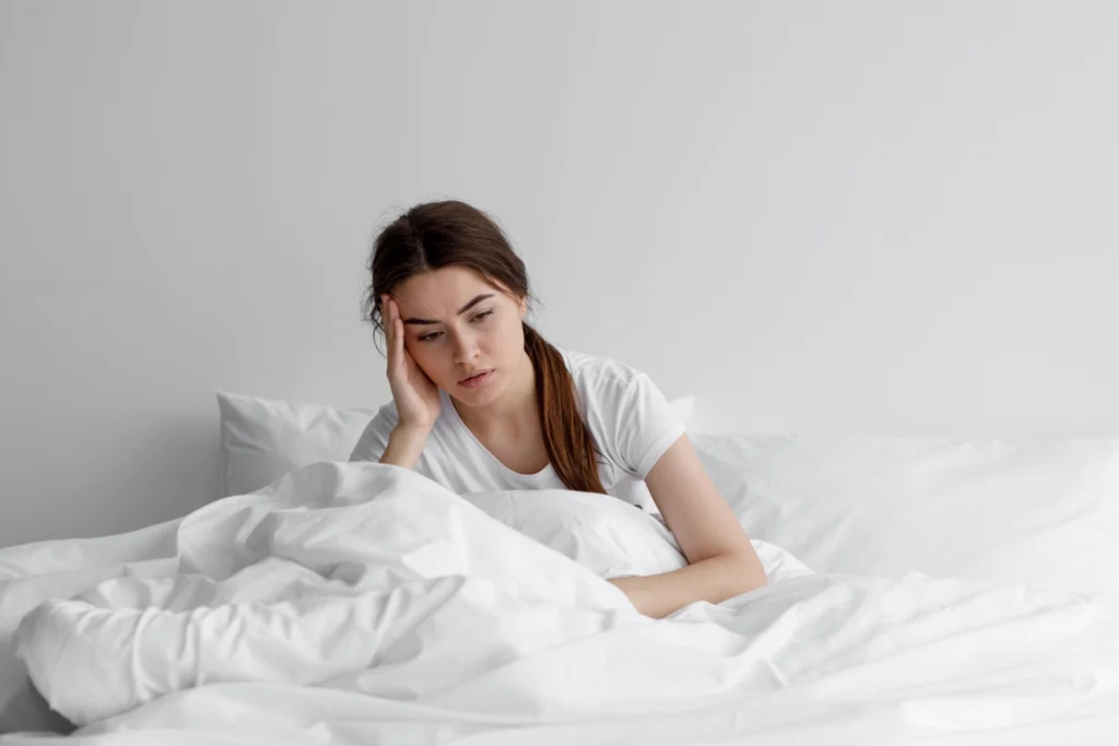 Woman on white bed looking sad from bad sleep.